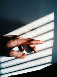 High angle view of sunlight falling on hand by wall
