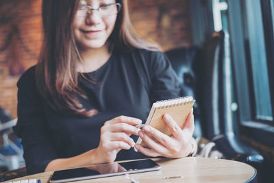 Woman writing in book by digital tablet on table