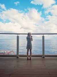 Rear view of woman standing by sea against sky