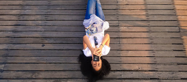 High angle view of woman using phone while lying on pier