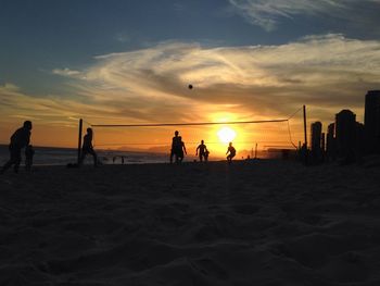 Silhouette people playing volleyball at beach against sky during sunset