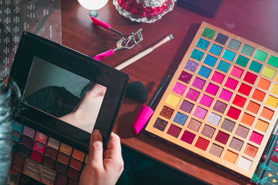 Woman in front of her dressing table holding her palette of colored eyeshadows that is worn out