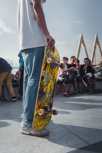 Midsection of man holding skateboard on street