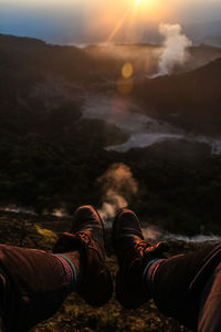 Low section of man sitting on cliff against landscape during sunset