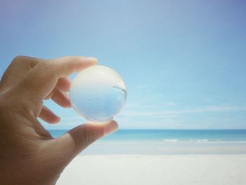 Human hand holding crystal ball on beach