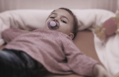 Portrait of girl lying on bed with pacifier in mouth at home