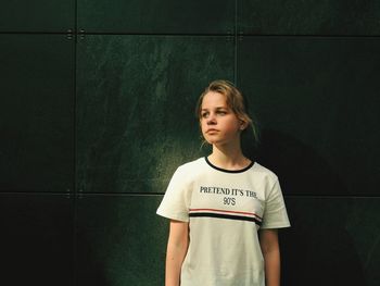 Teenage girl looking away while standing against wall