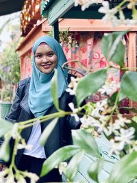 Portrait of smiling young woman wearing hijab standing by plants