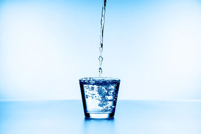 Close-up of glass pouring water against blue background