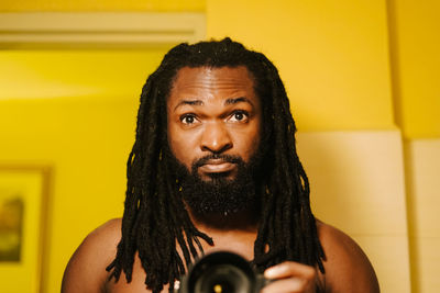 Close-up portrait of man with dreadlocks photographing against yellow wall