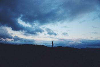 Silhouette person standing on hill against cloudy sky at dusk