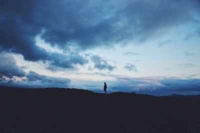 Silhouette of people on landscape against cloudy sky