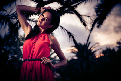 Young woman standing by tree against sky at night