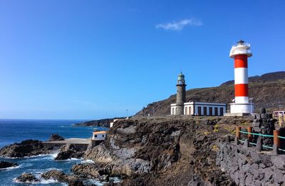 Lighthouse on beach by building against sky