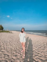 Full length of woman standing at beach against clear blue sky