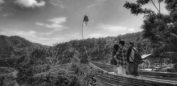 Rear view of people on road amidst trees against sky