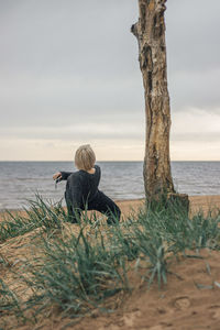 Rear view of man sitting at beach against sky