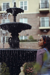 Teenage girl looking away by fountain in city