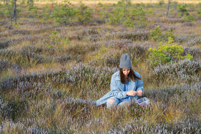 Young woman relaxes picking up ripe cranberries in autumn swamp grass alone