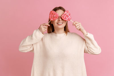 Woman holding lollipop against pink background