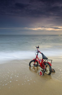 Bicycle on beach against sky during sunset