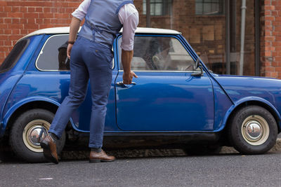 Low section of man opening car door on street