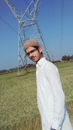 Portrait of boy standing on field against electricity pylon