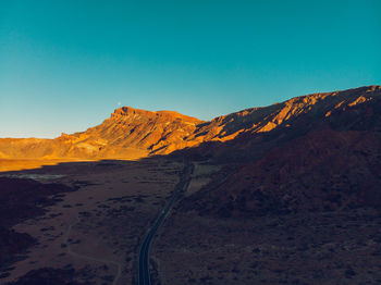 Scenic view of road amidst arid landscape against clear blue sky