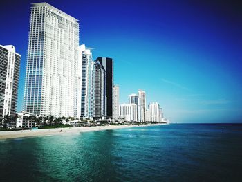 Sea by modern buildings against clear blue sky