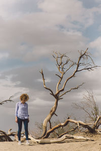 Young woman walking by fallen trees against sky at death valley national park