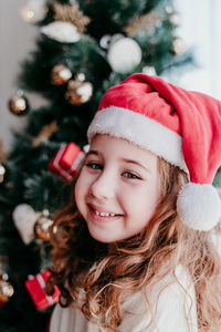 Portrait of smiling girl wearing santa hat by christmas tree