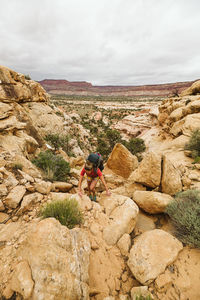 Female hiker scrambles up a rock face while hiking in canyonlands utah