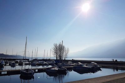 Sailboats moored in lake against sky on sunny day