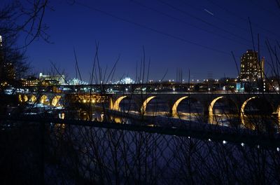 Arch bridge by river against sky in city at night