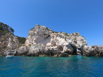 Scenic view of rocks in sea against clear blue sky