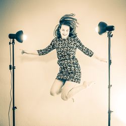 Smiling woman jumping by illuminated lights in studio