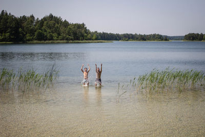 Shirtless men standing with arms raised in river