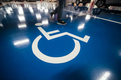 Low section of man walking on disabled sign over blue floor