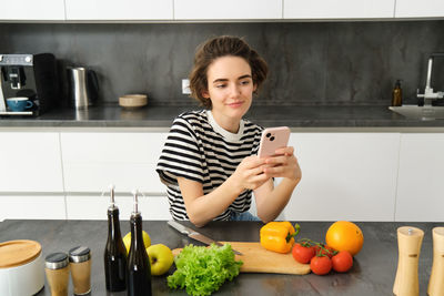 Portrait of young woman using mobile phone in kitchen