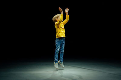 Happy candid caucasian little kid boy stands tall full height and jumps up and claps his hands