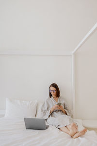 A european woman in a gray linen robe is working on a laptop at home or resting. a millennial woman