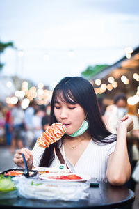 Portrait of young woman eating food on table at restaurant