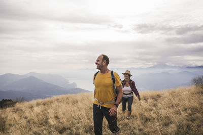 Happy mature man and woman hiking on mountain under cloudy sky