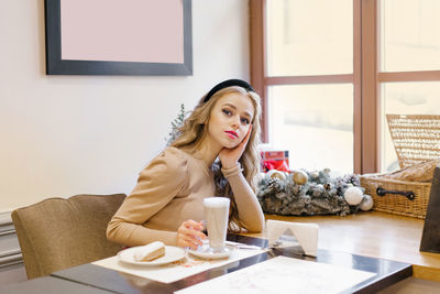 An attractive happy girl is sitting in a cafe decorated for christmas, drinking coffee and eating