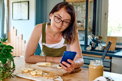 Woman enjoying her healthy breakfast checking on her smart phone at home.
