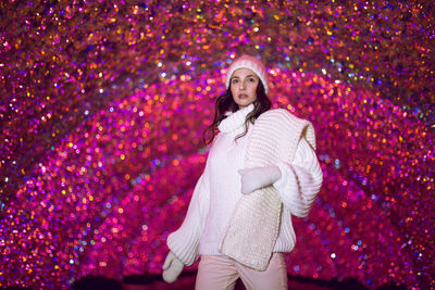 Woman in a white sweater, hat and white scarf on a background of pink lights