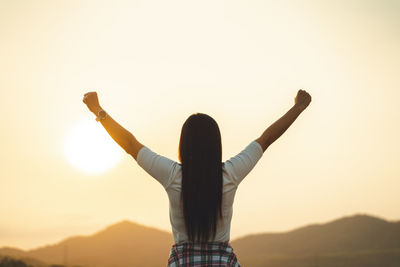 Rear view of woman with arms outstretched against sky during sunset