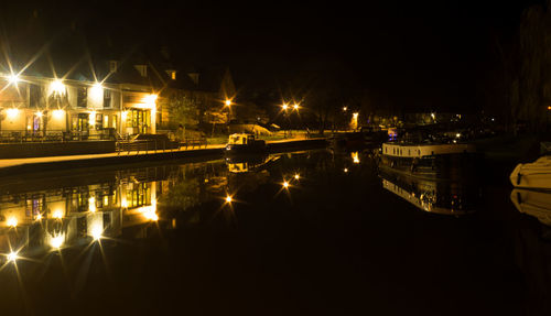 Illuminated city by river against sky at night