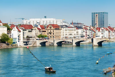 Bridge over river by buildings against clear sky