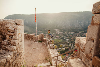 Woman sitting on retaining wall against mountain in town